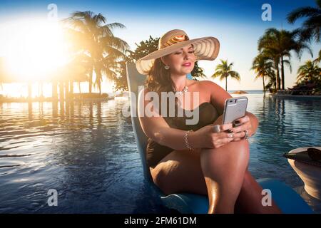 Wunderschöne kurvige Frau, die sich am Pool entspannt und an der Arbeit arbeitet Ihr Telefon Stockfoto