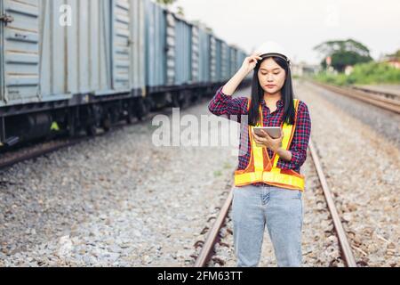 Porträt einer schönen Frau, die mit einem Tablet mit einem Hardhut vor der Zuggarage unterwegs war. Stockfoto