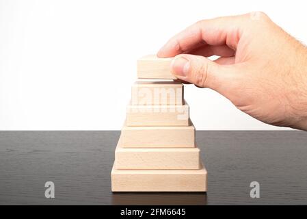 Nahaufnahme der Hand einer Person, die Holzblöcke stapelt und eine bildet Pyramidenform Stockfoto