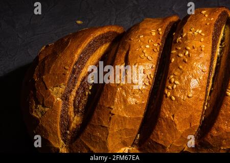 Ungewöhnlicher zweifarbiger frischer Laib Brot auf schwarzem Hintergrund, Foto in einer niedrigen Taste bei hartem Licht, Nahaufnahme Stockfoto