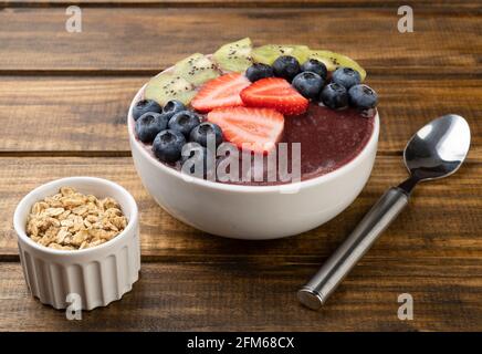 Brasilianische typische acai Schale mit Kiwi, Heidelbeere und Erdbeere über Holztisch. Stockfoto