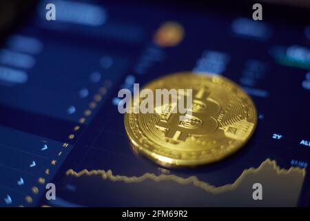 Die Goldbitcoin-Münze liegt auf dem Tablet-Bildschirm, der Veränderungen der Kryptowährungsraten anzeigt Stockfoto