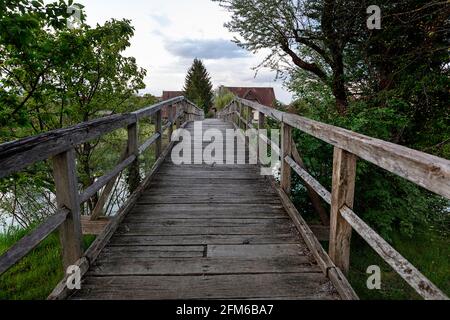 Hölzerne Fußgängerbrücke über den Fluss Krka in Slowenien, mit der umliegenden Kleinstadt Kostanjevica Stockfoto
