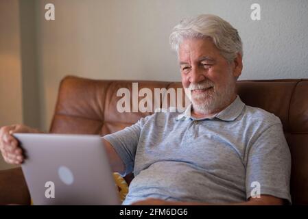 Glücklicher Mann im Innenbereich, der am Laptop arbeitete und lächelte, entspannte ältere Männer, die im Internet surfen oder Computersurfen, Nachrichten online lesen und aufgeregt im Feld waren Stockfoto
