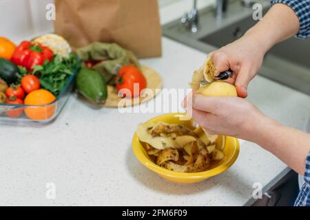 Lebensmittelverlust und Lebensmittelverschwendung. Reduzierung Von Lebensmittelverschwendung Zu Hause. Lösung des Problems der Lebensmittelverschwendung. Weibliche Hände schälen Kartoffeln, Kartoffelschälen in einer Schüssel Stockfoto