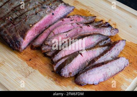 Bourbon mariniertes gegrilltes Flankensteak: In Scheiben geschnittenes, mittelseltenes Flankensteak auf einem Bambusschnitzbrett Stockfoto