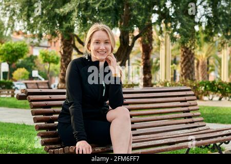 Porträt einer jungen blonden Frau, die die Kamera anlächelt In einem Park Stockfoto