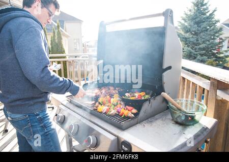 Mann grillen Huhn und Gemüse im Freien auf einem Gas-bbq-Grill. Stockfoto