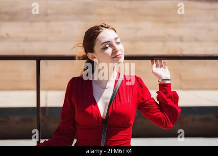 Junge rothaarige Frau genießt die Sonne in der Stadt. In einer roten Bluse gekleidet. Stockfoto