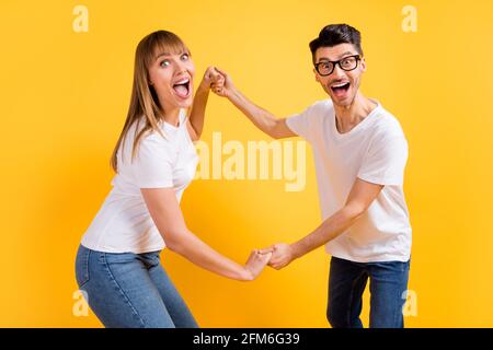 Foto von ziemlich aufgeregt junge Paar tragen weiße T-Shirt Brille Halten Sie die Hände Arme tanzen isoliert gelben Hintergrund Stockfoto