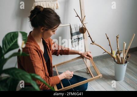 Seitenansicht einer Frau, die einen Wollteppich webt, auf dem sie sitzt Der Boden Stockfoto