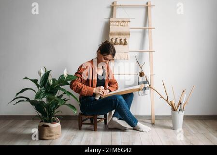 Junge Frau bereitet Rahmen für Woll Weberei Sitz auf einem Kleiner Hocker Stockfoto
