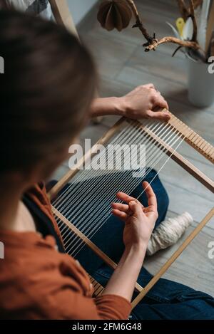 Rückansicht der Frau, die den Rahmen für das Weben von Wollteppich vorstellt Stockfoto