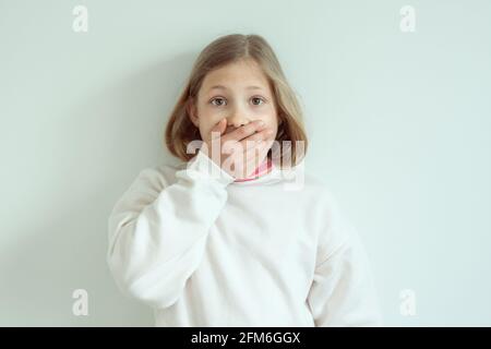 Erstauntes lustiges kleines Mädchen mit weit offenen Augen schloss sie Mund mit der Hand Stockfoto