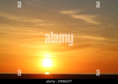 Blick auf den Sonnenuntergang über der Bucht von Morecambe mit Windturbinen am Horizont über Pilling Sands von Fluke Hall in Pilling, Lancashire, England. Stockfoto