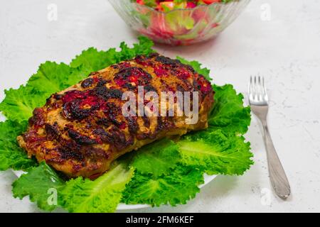 Ein großes Stück Schweinefleisch, im Ofen gekocht, im Ofen gebacken, auf grünen Salatblättern. Mit Pasta auf einem Teller mit einer Gabel und einem Messer. Gegen die Stockfoto