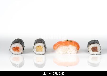 Drei Maki-Rollen und ein Lachs-Nigiri in einer Reihe isoliert auf weißem Hintergrund. Frische Hosomaki-Stücke mit Reis und Nori. Nahaufnahme von leckeren japanischen fo Stockfoto