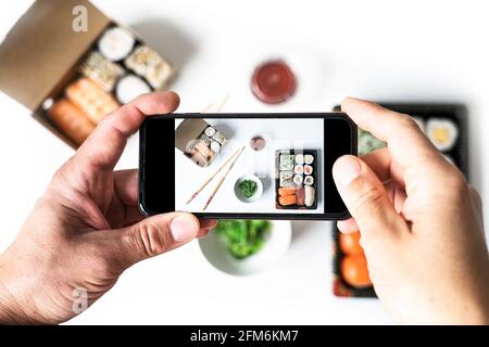 Draufsicht auf einen Mann, der Sushi auf dem weißen Tisch fotografiert. Social Networking und Take-away-Konzept Stockfoto