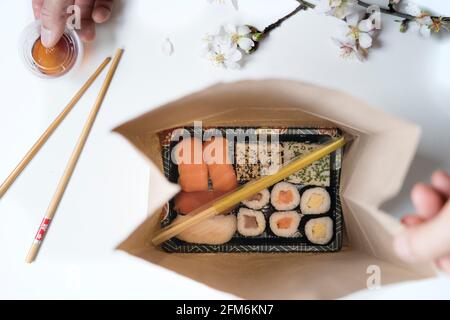 Draufsicht auf eine Take-Away-Box mit Sushi-Rollen und Essstäbchen in einem braunen, recycelbaren Papierbeutel. Konzept für die Lieferung von Lebensmitteln. Stockfoto
