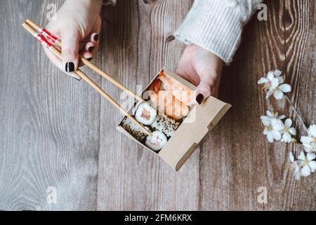 Selektiver Fokus auf Lebensmittel. Draufsicht auf eine Frau, die asiatische Speisen zum Mitnehmen mit Essstäbchen auf einem Holztisch isst. Home Delivery-Konzept. Stockfoto