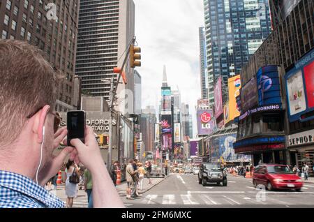 Ein Tourist macht ein Foto mit seinem Telefon auf der 42. Straße am Times Square in New York City, NY. Stockfoto