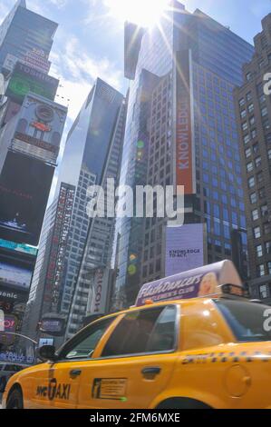 Ein NYC-Taxi, bekannt als gelbes Taxi, fährt durch den Times Square. Die hohen Gebäude ragen über den Straßen der Stadt. Stockfoto