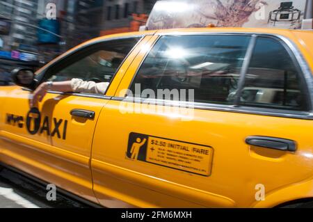 Ein NYC-Taxi, bekannt als gelbes Taxi, fährt durch den Times Square. Der Fahrer hat seinen Arm aus dem Fenster gehängt. Stockfoto