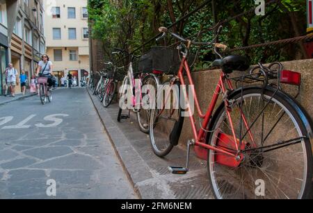 Mehrere einstufige Fahrräder fahren entlang der Via de ramaglianti, einer Straße in Florenz, Italien. Es gibt zwei rote, eine rosa und weiße, und eine weiße geparkt Stockfoto