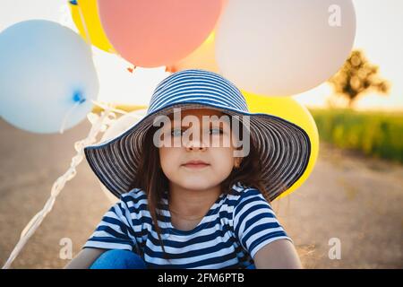 Kleines Mädchen auf der Straße mit bunten Ballons in den Händen sitzen Bei Sonnenuntergang Stockfoto