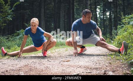 Kaukasische Frau und Mann tun Bein Stretching-Übungen in der Wald Stockfoto