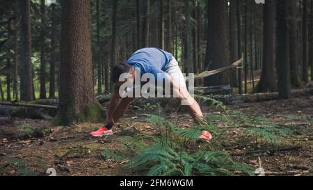 Breite Aufnahme von kaukasischen Mann in Sportkleidung tun Beine und Rückendehnungs-Übungen im Wald Stockfoto