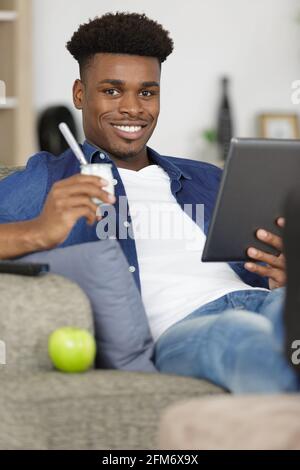 Mann auf dem Sofa mit einem Tablet und einem Joghurt in der Hand Stockfoto