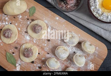 Kochen von hausgemachten Knödeln, russischen Knödeln mit Fleisch auf einem Holztisch und Zutaten zum Kochen. Rustikaler Stil. Draufsicht Stockfoto