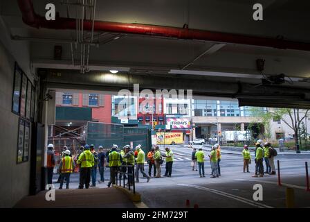 Eine große Gruppe von Bauherren, die persönlichen Schutz tragen, warten auf der Straße, um ihre Arbeit zu beginnen. Stockfoto