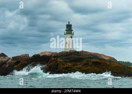 Die Wellen brechen am alten Turm des Moose Peak Leuchtturms auf einer felsigen Insel, an einem bewölkten Tag, an dem die Sonne durch Sturmwolken in Maine bricht. Leuchttürme von Nort Stockfoto