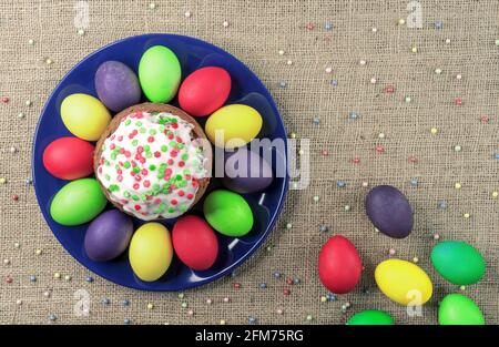 Runder Teller mit bunten Ostereiern und Osterkuchen auf einem Sackleinen-Hintergrund. Stockfoto