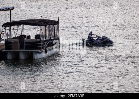 Guatapé, Antioquia, Kolumbien - April 3 2021: Lateinischer Mann fährt einen Jetsky in der Nähe eines Bootes auf dem See in Guatape Marina in Dusk Marina in Dusk Stockfoto