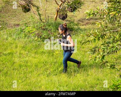 Junge kurze hispanische Frau in blauer Jeans und schwarzem Shirt Nimmt Bilder mit der kompakten, spiegellosen Kamera auf Stockfoto