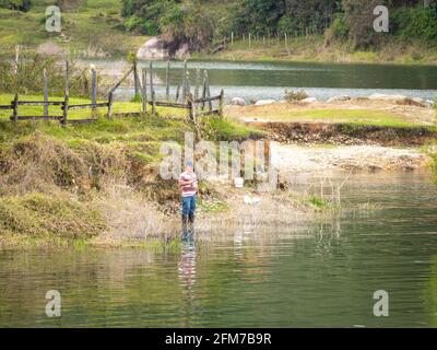 Guatape, Antioquia, Kolumbien - April 4 2021: Alter Mann in blauer Jeans und schwarzen Stiefeln Fliegenfischen am Flussufer Stockfoto