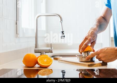 Junge Hände quetschen Orangen in einem Handbuch aus Edelstahl Entsafter auf einem Holztisch in der Küche Mit Küchenarmatur in natürlichem Licht Stockfoto