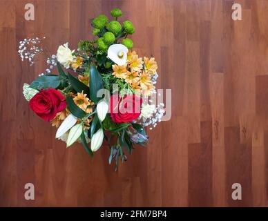 Draufsicht auf einen Blumenstrauß mit Rosen, Calla-Lilien, Gänseblümchen und Nelken, auf einem Holzboden, selektiver Fokus auf den Strauß, Kopierraum, Horizont Stockfoto