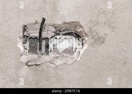 Nische für die Installation mehrerer Steckdosen an einer grauen Betonwand, Hausreparatur. Stockfoto