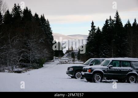 Autos parkten in EINER schneebedeckten Auffahrt durch EINEN Wald, mit Rolling Hills im Hintergrund Stockfoto