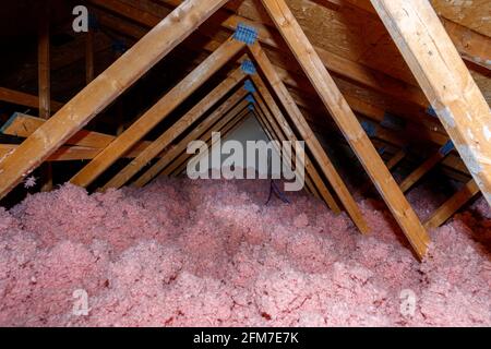 Ein dunkler Dachboden in einem Holzhaus verfügt über eine rosafarbene, lose ausgefüllte Glasfaserisolierung, die den Boden bedeckt. Stockfoto