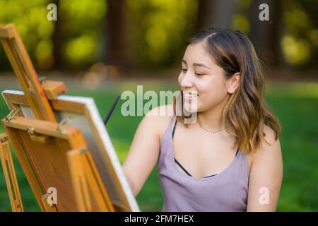 Petite junge asiatische Frau Student Malerei im Park mit Ein Kabinett-Easel Stockfoto