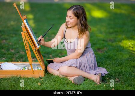 Petite junge asiatische Frau Student Malerei im Park mit Ein Kabinett-Easel Stockfoto