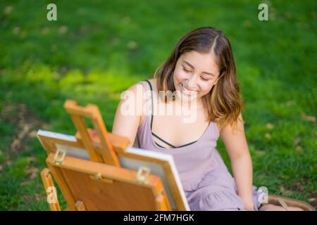 Petite junge asiatische Frau Student Malerei im Park mit Ein Kabinett-Easel Stockfoto