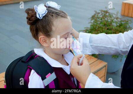 Mutter setzt ihre Töchterschutzmaske vor der Schule auf. Schülerin. Neuer Normalwert. Coronavirus-Schutz Stockfoto