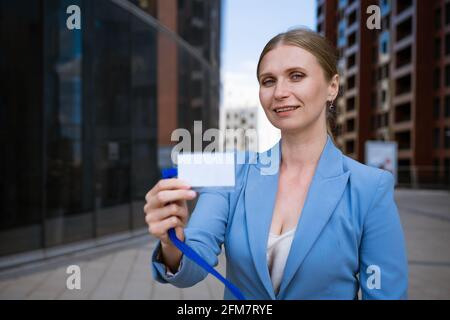 Business stilvolle Frau in einer blauen Jacke hält ein Abzeichen In der Hand vor dem Hintergrund eines Bürogebäudes Stockfoto