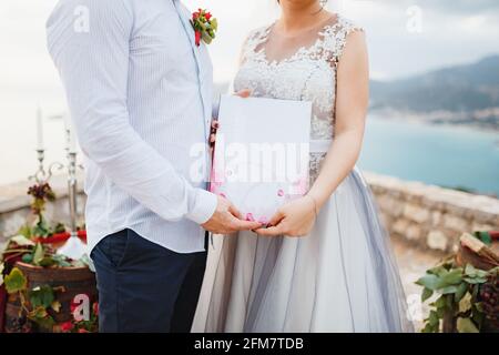 Die Braut und der Bräutigam umarmen und halten eine Heiratsurkunde in ihren Händen, aus nächster Nähe Stockfoto